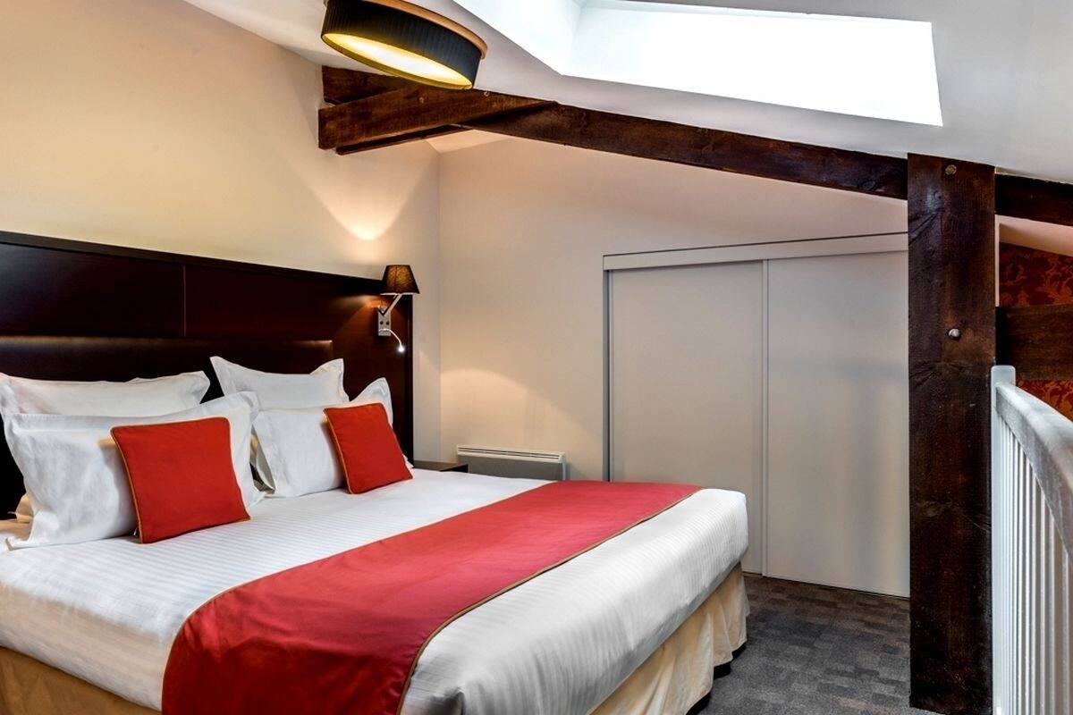 Una habitación de hotel con una cama grande, tragaluces, cabecera de madera y un armario blanco.