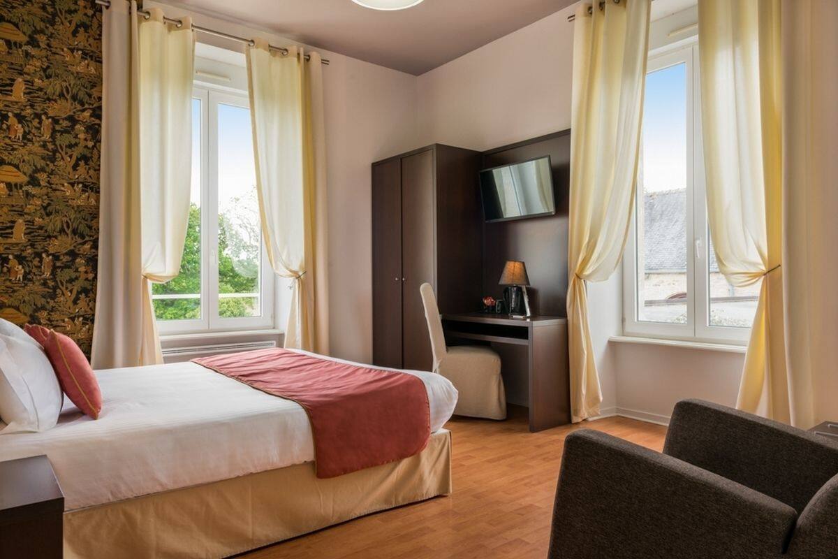 Una habitación de hotel con cama, escritorio, silla, televisor y ventana con cortinas.