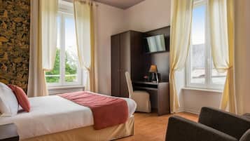 Een hotelkamer met een bed, bureau, stoel, televisie en een raam met gordijnen.
