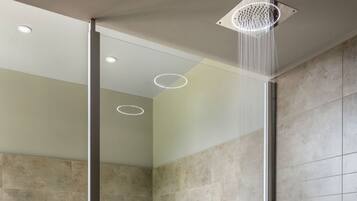 A modern bathroom with a glass-enclosed shower, a built-in bathtub, and a wooden staircase.