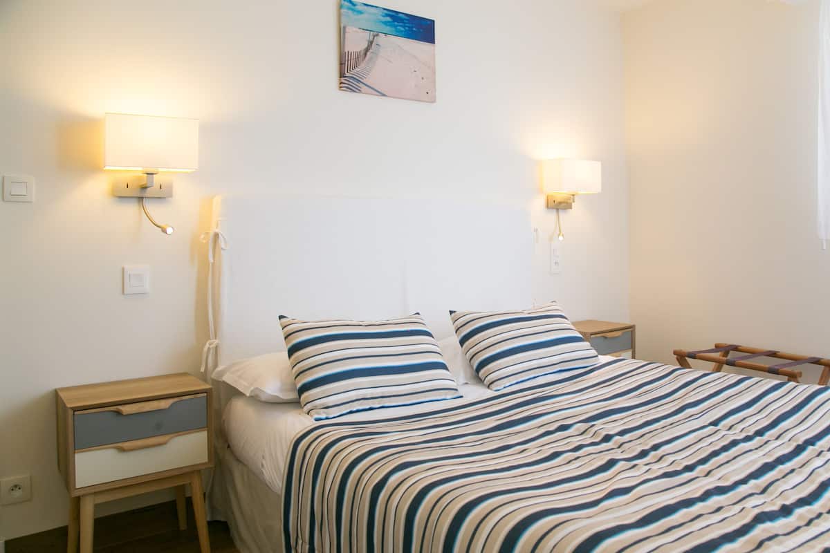 Una cama con ropa de cama a rayas, dos mesitas de noche con lámparas, una mesita de noche de madera y un cuadro colgado en la pared.