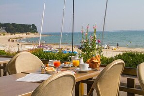 An outdoor dining area with a table set for breakfast, overlooking a beach and the sea. - Hotel De la Plage (Saint-Pierre-Quiberon)