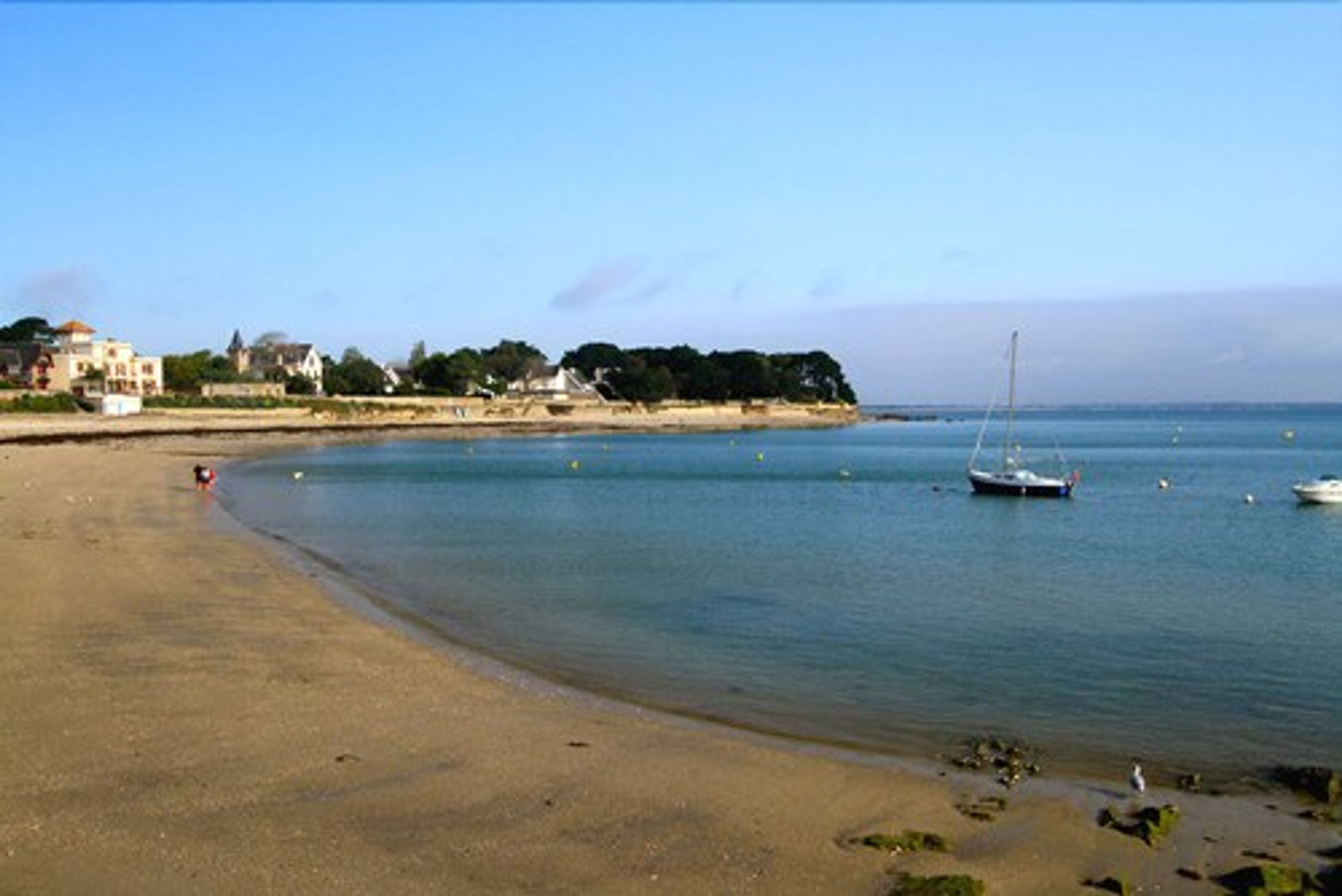A beach with a sandy shore, calm water, and a sailboat.