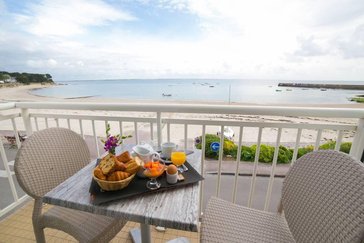Un balcón con sillas de mimbre, una mesa con alimentos para el desayuno y vista a la playa y al mar.