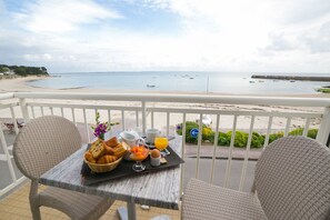 Un balcon avec des fauteuils en osier, une table avec des aliments pour le petit-déjeuner et une vue sur la plage et la mer.