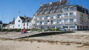 Een hotel met meerdere verdiepingen, balkons, een restaurant en een strand op de voorgrond.