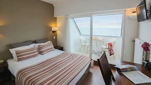 Hotelkamer met een bed, een bureau, een stoel en uitzicht op zee door een glazen deur.