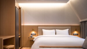 Et moderne hotelværelse med en stor seng, træsenggavl, sengeborde med lamper og et indbygget klædeskab.