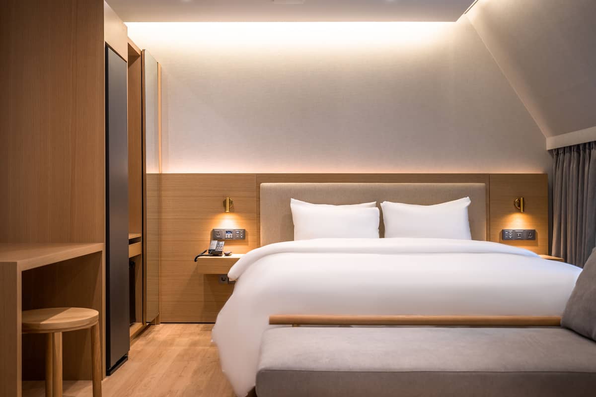Habitación de hotel moderna con una cama grande, cabecera de madera, mesitas de noche con lámparas y un armario empotrado.