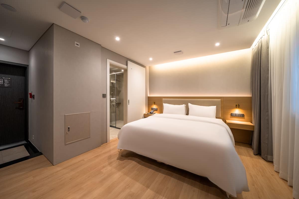 Una habitación de hotel moderna con una cama grande, mesitas de noche, un armario y un baño visible a través de una puerta abierta.