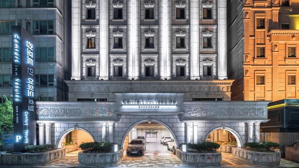En hotels facade i klassisk arkitekturstil, med en central indgang prydet med søjler og et skilt over døren.