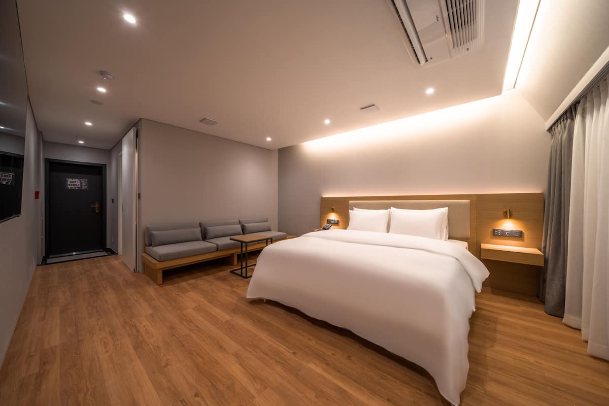 Una habitación de hotel moderna con una cama grande, un sofá, una mesita y una mesita de noche con lámpara.