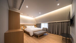Una habitación de hotel moderna con una cama grande, mesitas de noche, un banco y un televisor fijado a la pared.