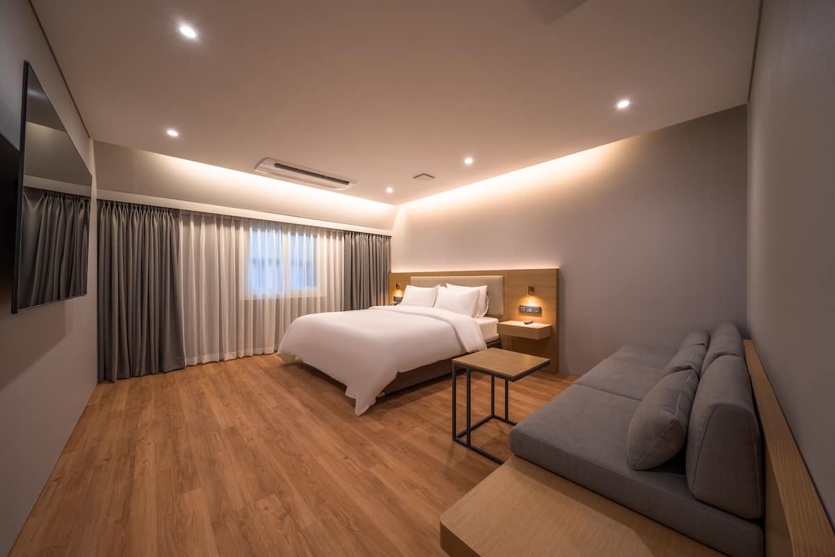 Una habitación de hotel moderna con una cama grande, un sofá, una mesita y un televisor montado en la pared.