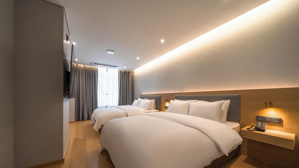 Una habitación de hotel con dos camas, una mesita de noche con teléfono e iluminación en la pared.