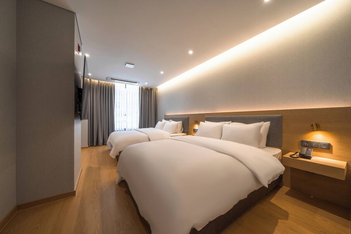 Una habitación de hotel con dos camas, una mesita de noche con teléfono e iluminación en la pared.