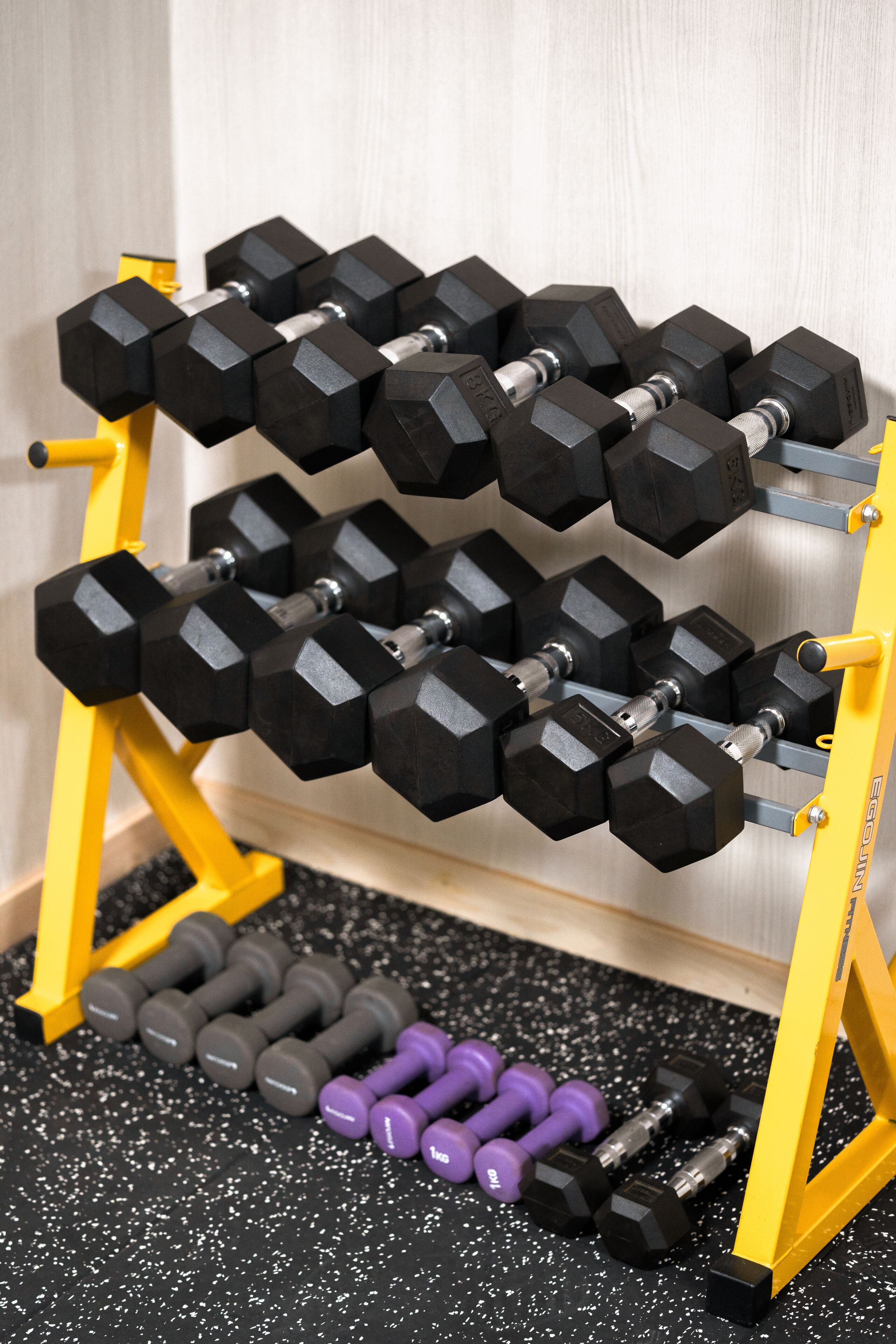 A set of dumbbells on a rack with a speckled floor.