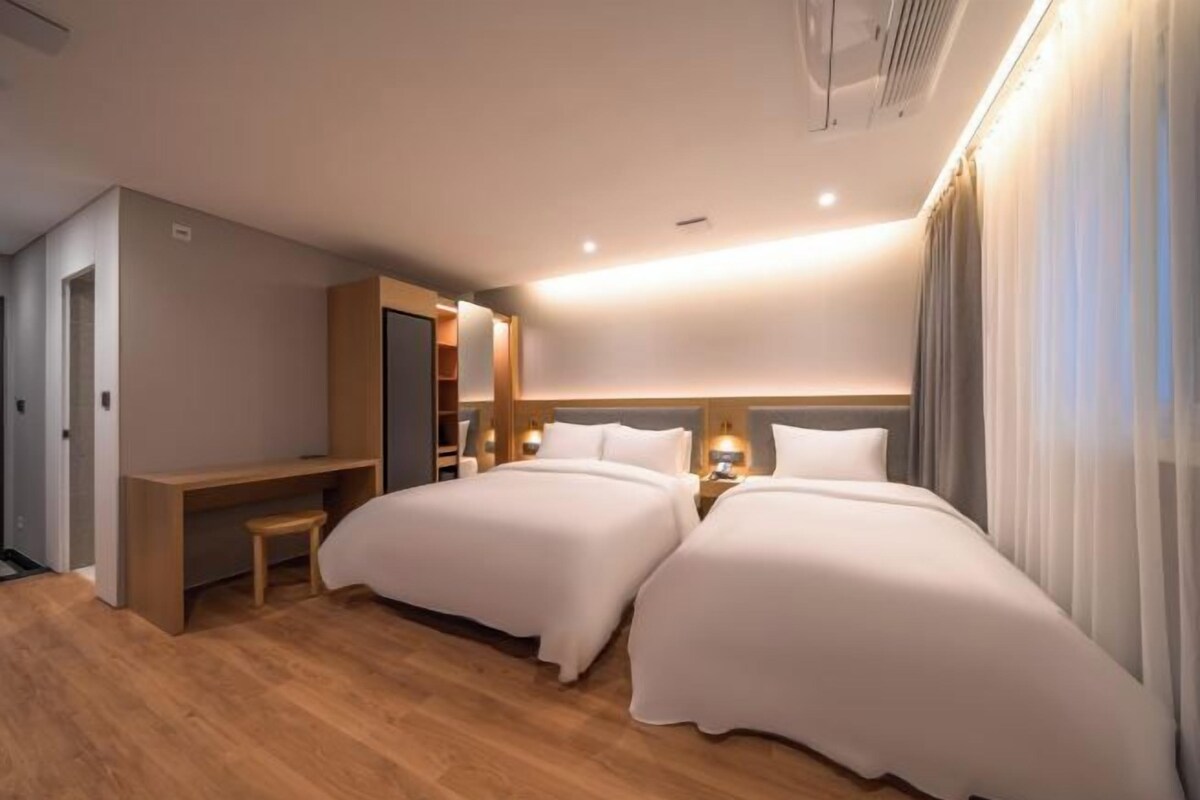A hotel room with two beds, a desk, and a wardrobe.
