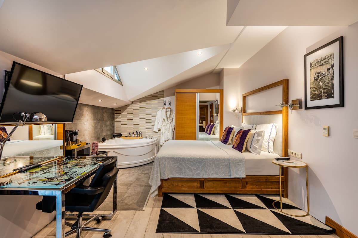 A modern bedroom with a bed, a desk, and a large window.