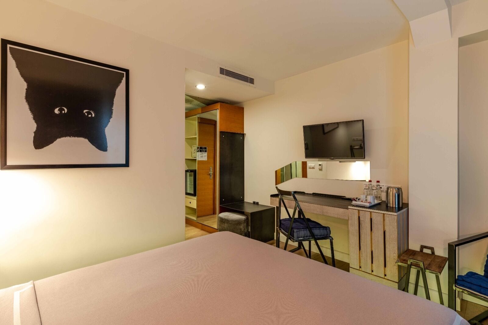 Ein Hotelzimmer mit einem Bett, einem Schreibtisch, einem Sessel, einem Fernseher und einem Katzenbild.