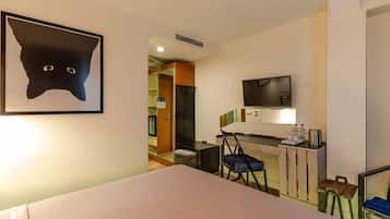 Ein Hotelzimmer mit einem Bett, einem Schreibtisch, einem Sessel, einem Fernseher und einem Katzenbild.