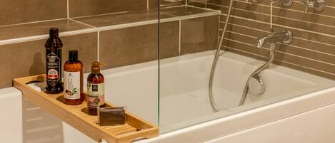 A bathroom with a bathtub, a wooden shelf with toiletries, and a glass shower enclosure.