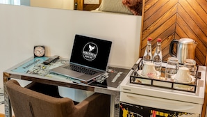 Un espacio de trabajo en un hotel con una computadora portátil, un reloj, una bandeja con botellas y vasos, y una cafetera.
