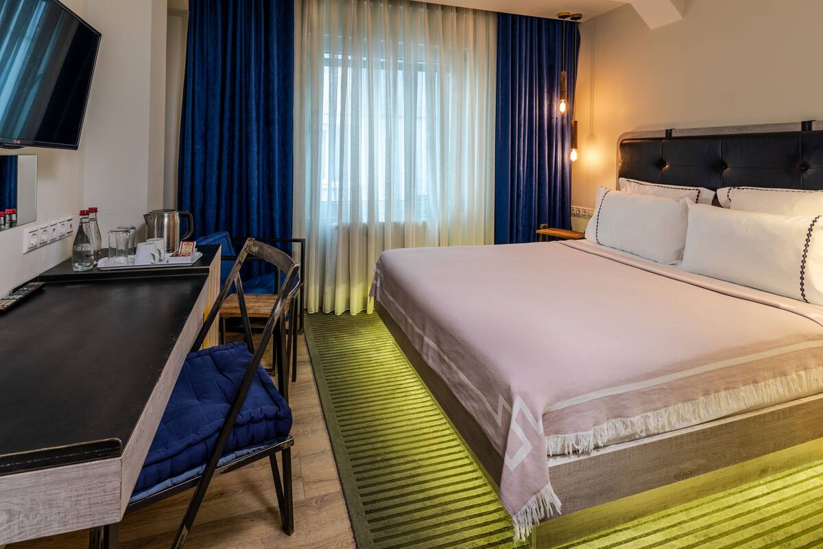 A hotel room with a bed, a desk with a chair, a television, and a window with curtains.