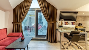 Una habitación moderna con un sofá rojo, una mesa de vidrio, un escritorio con una silla y un ventanal con cortinas.