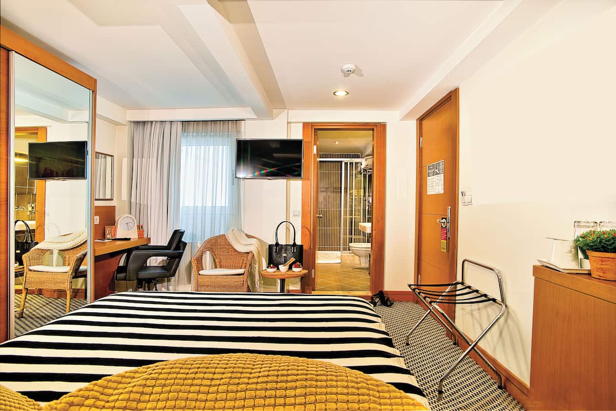 A hotel room with a bed, a desk with a chair, a television, a bathroom, and a small table with a handbag.
