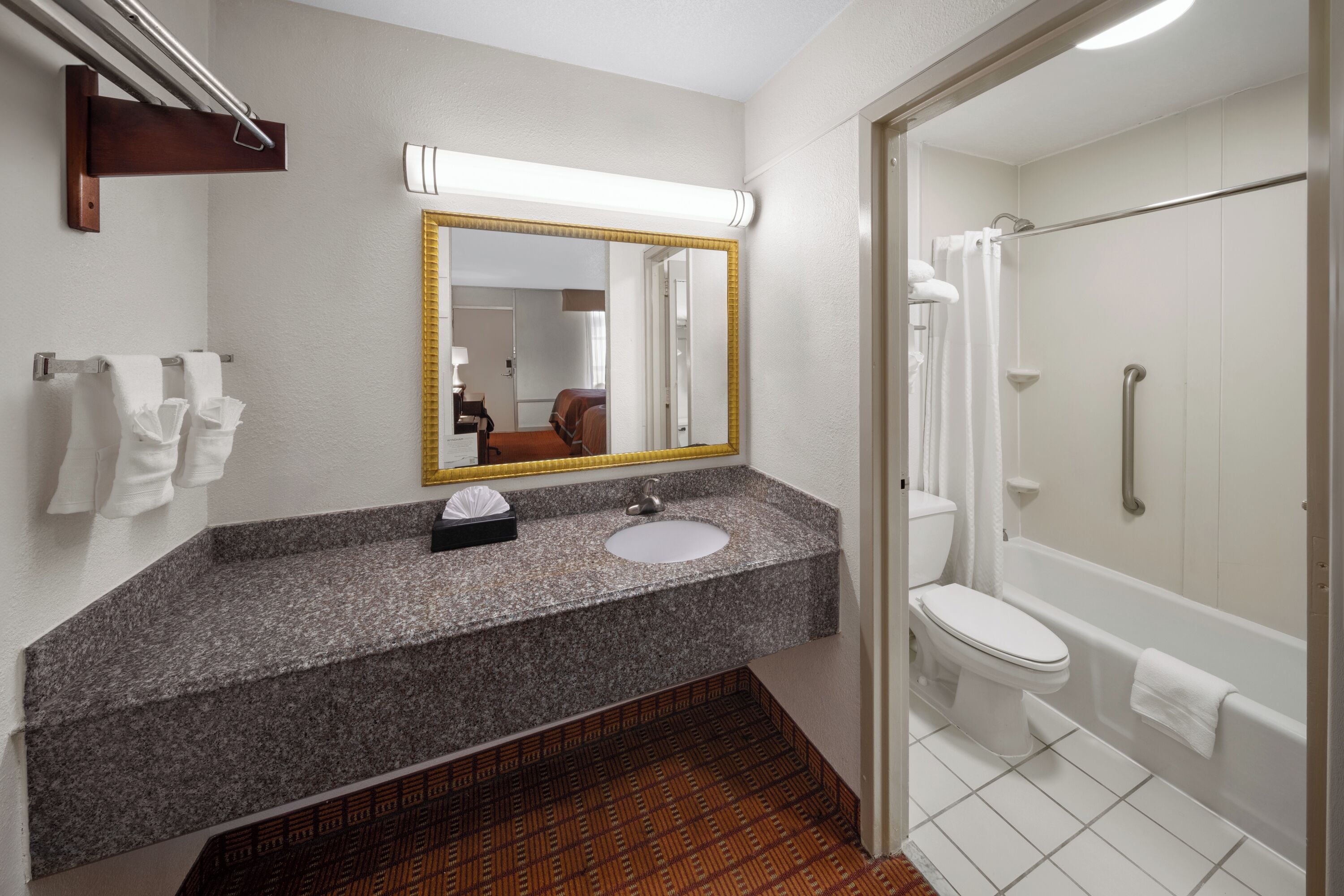 Een badkamer met een wastafel met een granieten blad, een spiegel, een toilet en een douche.
