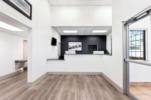 Un área de recepción con mostrador, televisor montado y un cuadro en la pared.