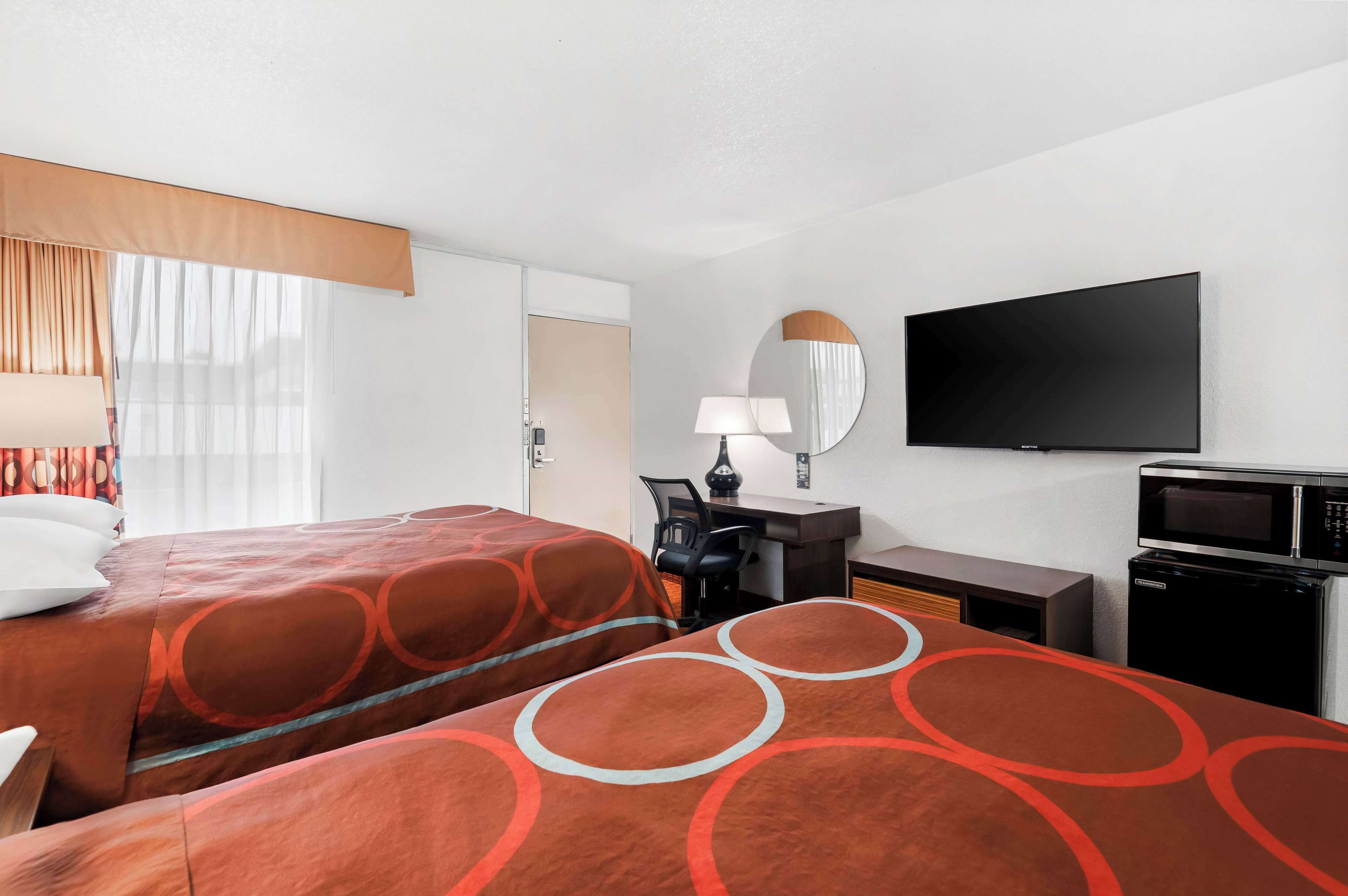 A hotel room with two beds, a desk with a chair, a flat-screen TV, a microwave, and a small refrigerator.