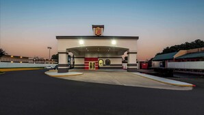 A gas station with a prominent '7-Eleven' sign, a covered entrance, and a clear sky.