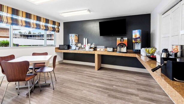 A modern kitchen with a dining area, featuring a large window, a flat-screen TV, and various kitchen appliances.