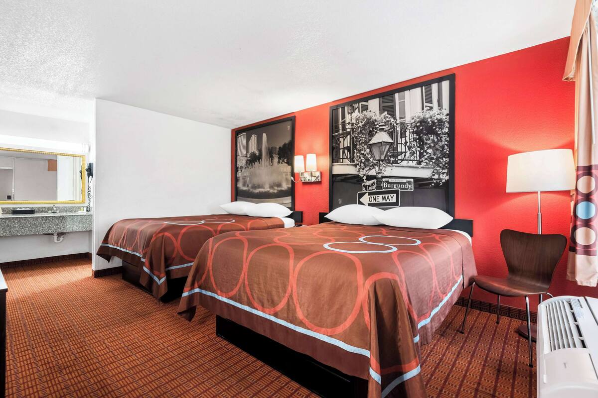 A hotel room with two beds, a mirror, a desk, a chair, and a wall with a black and white photo.