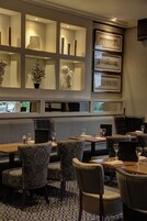 Un restaurante con zona de estar que incluye cabinas acolchadas y mesas, suelo estampado y estanterías con obras de arte enmarcadas y objetos decorativos.