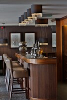 Zona de bar con mostrador de madera, varios taburetes y lámparas colgantes.