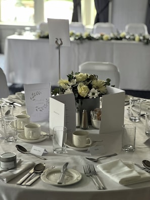 Une table dressée pour un événement formel, avec des nappes blanches, de la vaisselle transparente et un centre de table composé de fleurs.