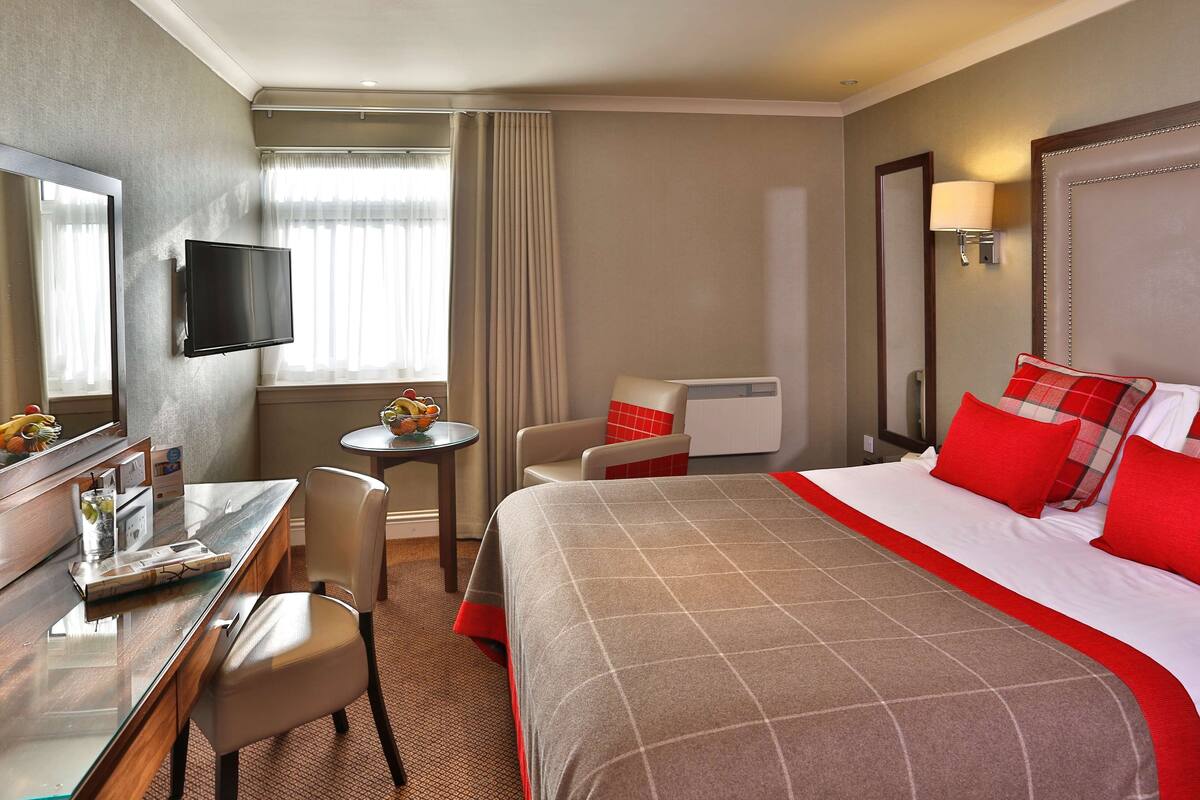 A hotel room with a bed, a desk, a chair, a television, and a window with curtains.