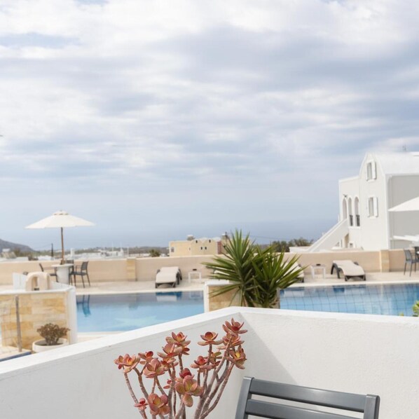 A rooftop pool area with lounge chairs, a white building with arched windows, and a clear sky. - Star (Santorini)