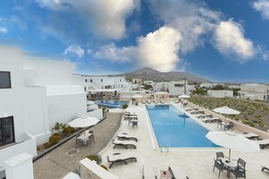 Zona de piscina en la azotea con sillones de descanso y sombrillas, rodeada de edificios blancos y una montaña al fondo.