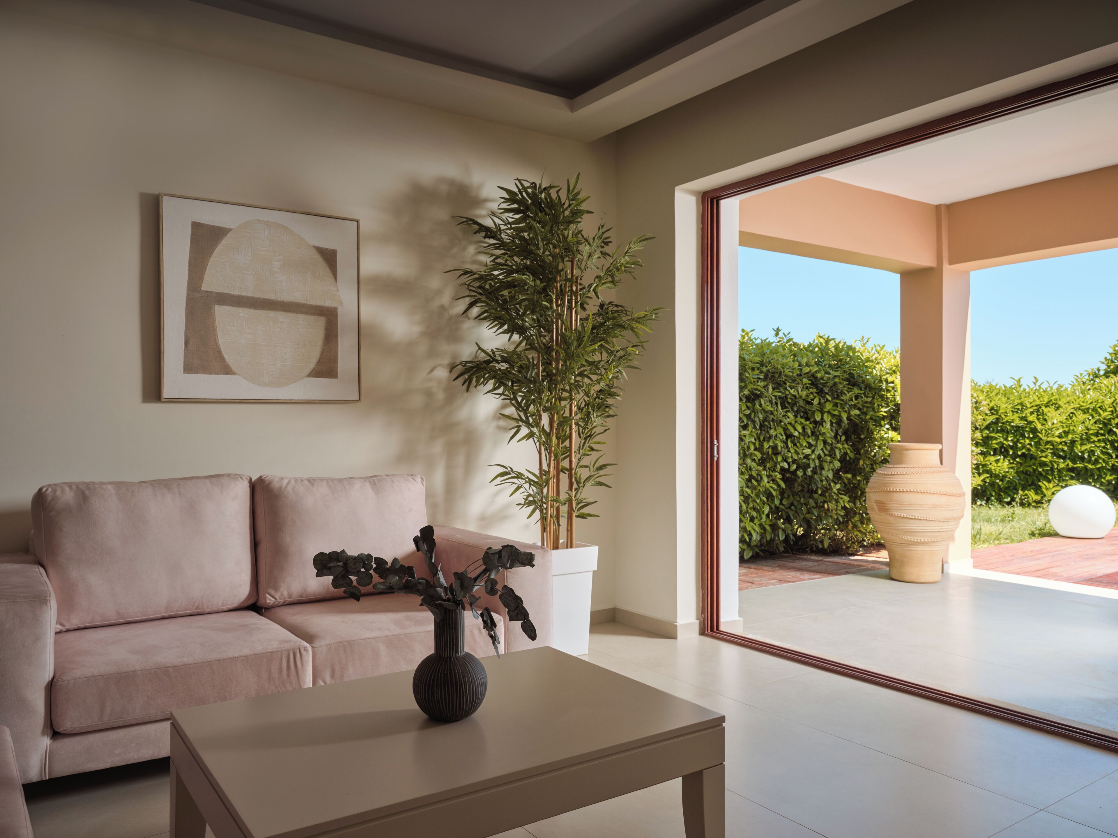 A modern living room with a sofa, a coffee table, a potted plant, and a large window.