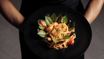 A person holding a black plate with a pasta dish, garnished with basil leaves.
