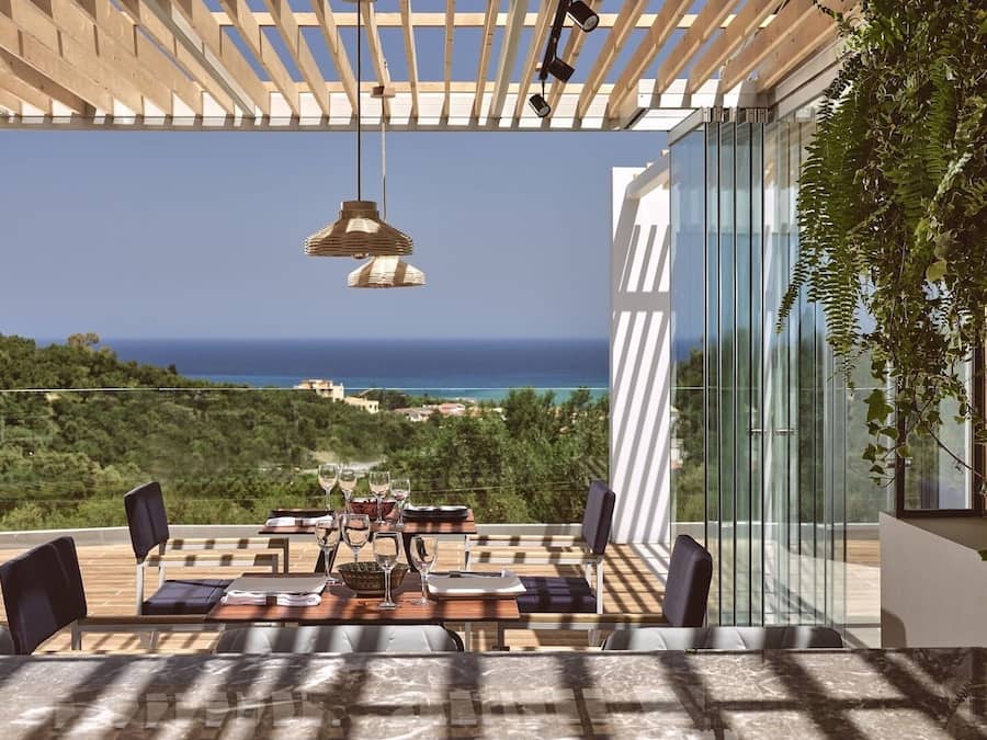 A terrace with a table set for dining, overlooking a coastal landscape.