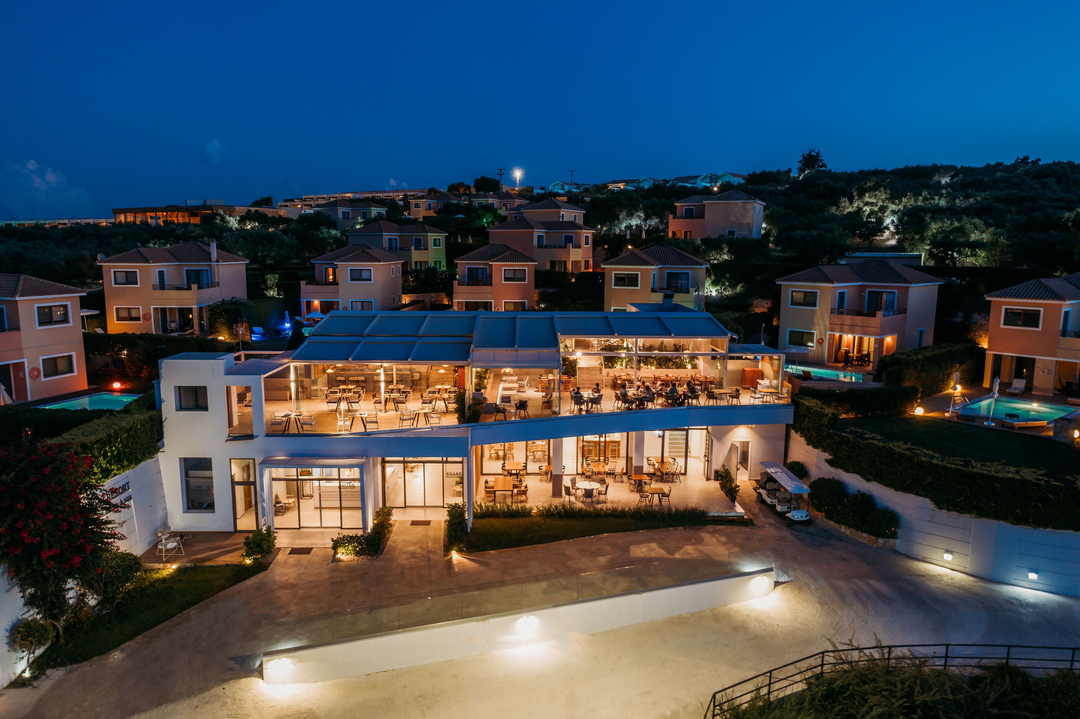 A multi-story hotel with a rooftop pool, outdoor seating area, and a well-lit entrance.