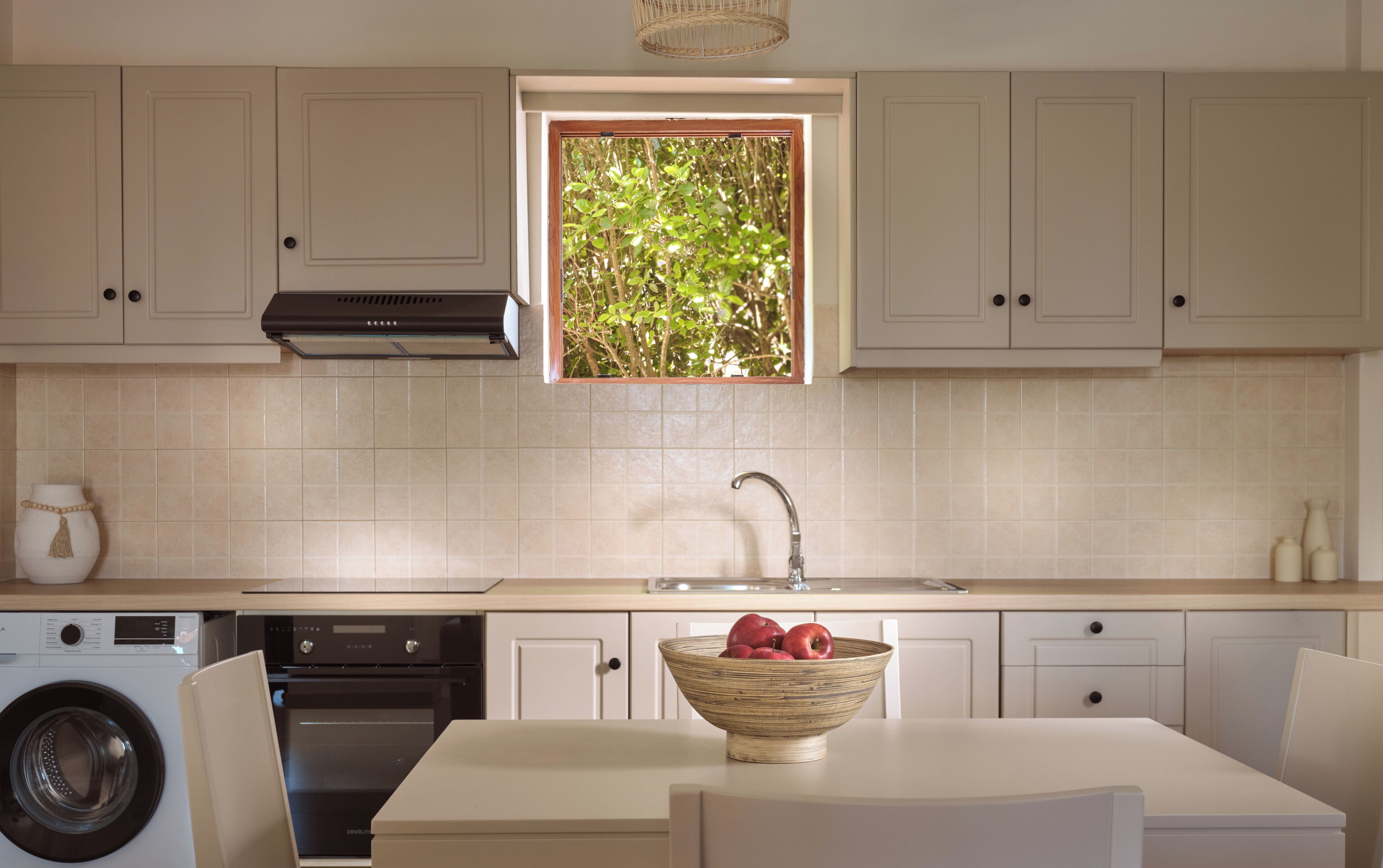 A kitchen with a built-in washing machine, a sink, and a window with a view of greenery.