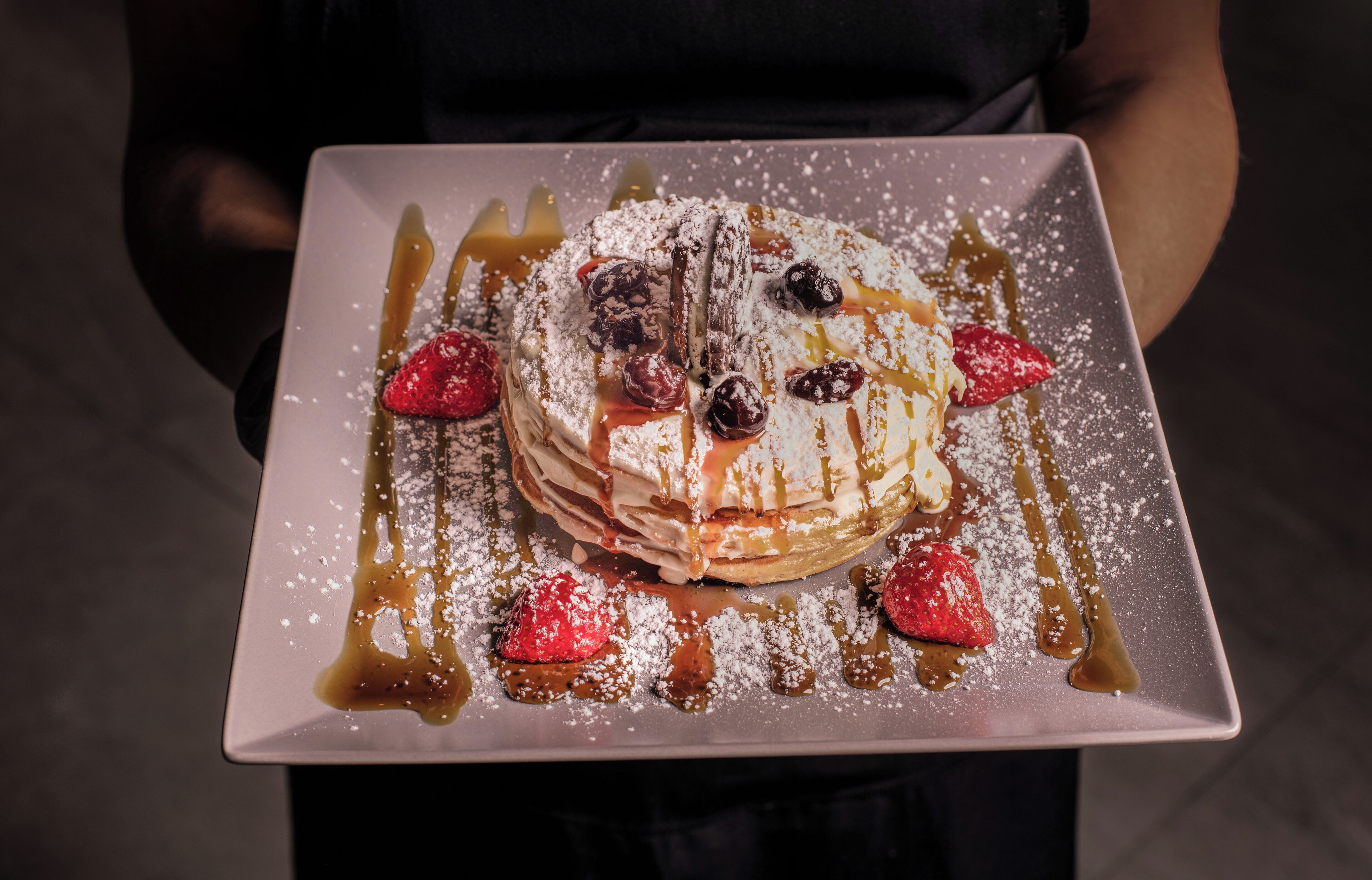A dessert plate with a stack of pancakes, berries, and syrup.