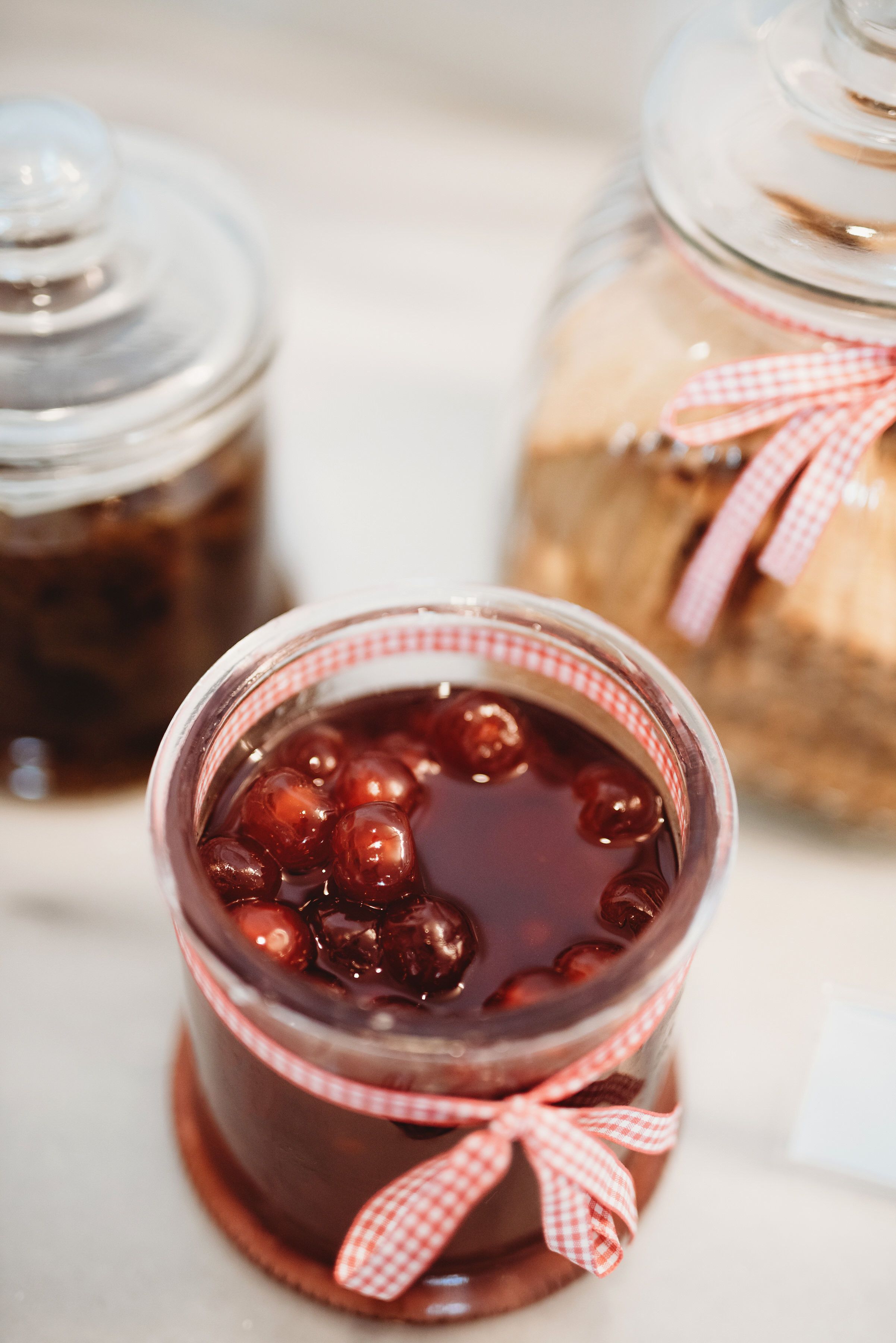Ein Glas dunkelrote Marmelade mit einem karierten Band auf einer weißen Oberfläche.