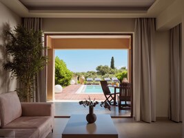 Un soggiorno moderno con un divano, un tavolino da caffè con un vaso e vista su un'area piscina esterna con lettini.